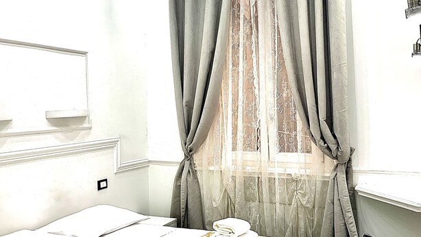 A hotel room with a neatly made bed, a window with curtains, a flat-screen TV, and a ceiling light fixture. - Antica Locanda dell'Orso (Rome)