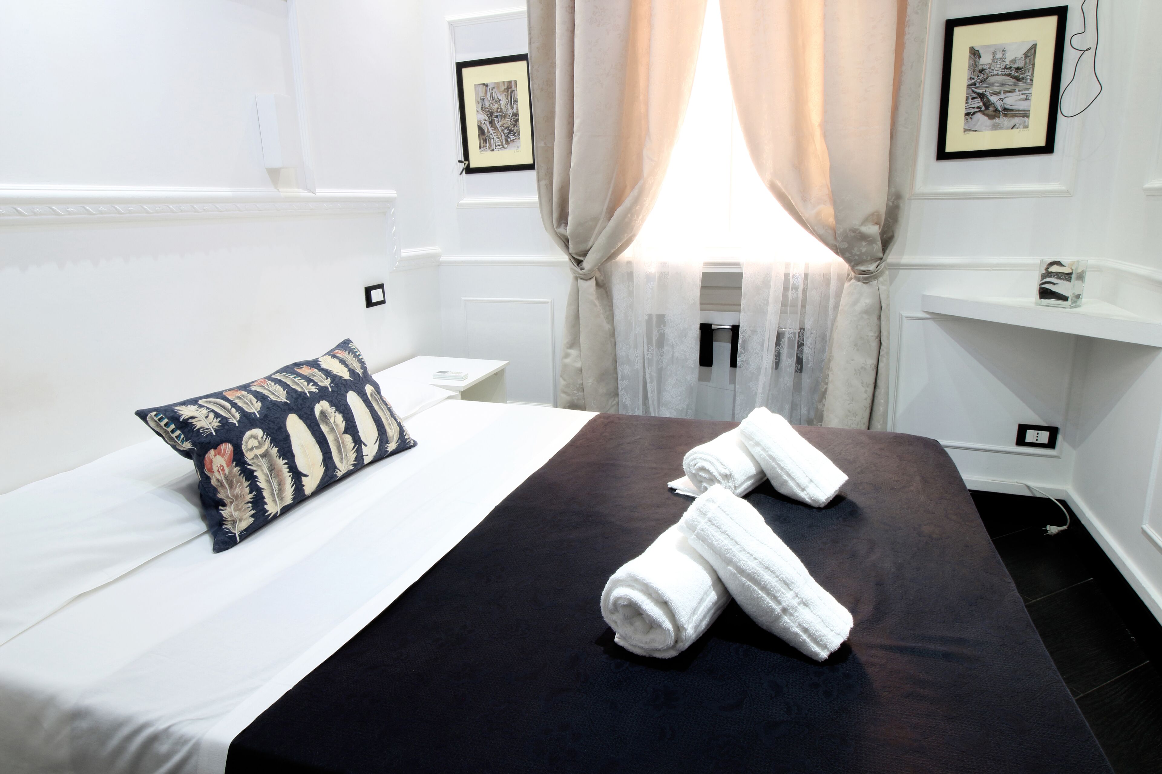 Habitación de hotel con cama, almohada, toallas, ventana con cortinas e imágenes enmarcadas en la pared.