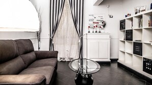 A modern living room with a brown leather sofa, a glass coffee table, a white bookshelf, and a black and white striped curtain. - Antica Locanda dell'Orso (Rome)