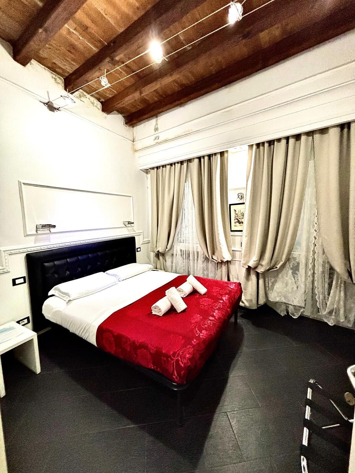 A hotel room with a large bed, a wooden ceiling, and curtains on the windows.