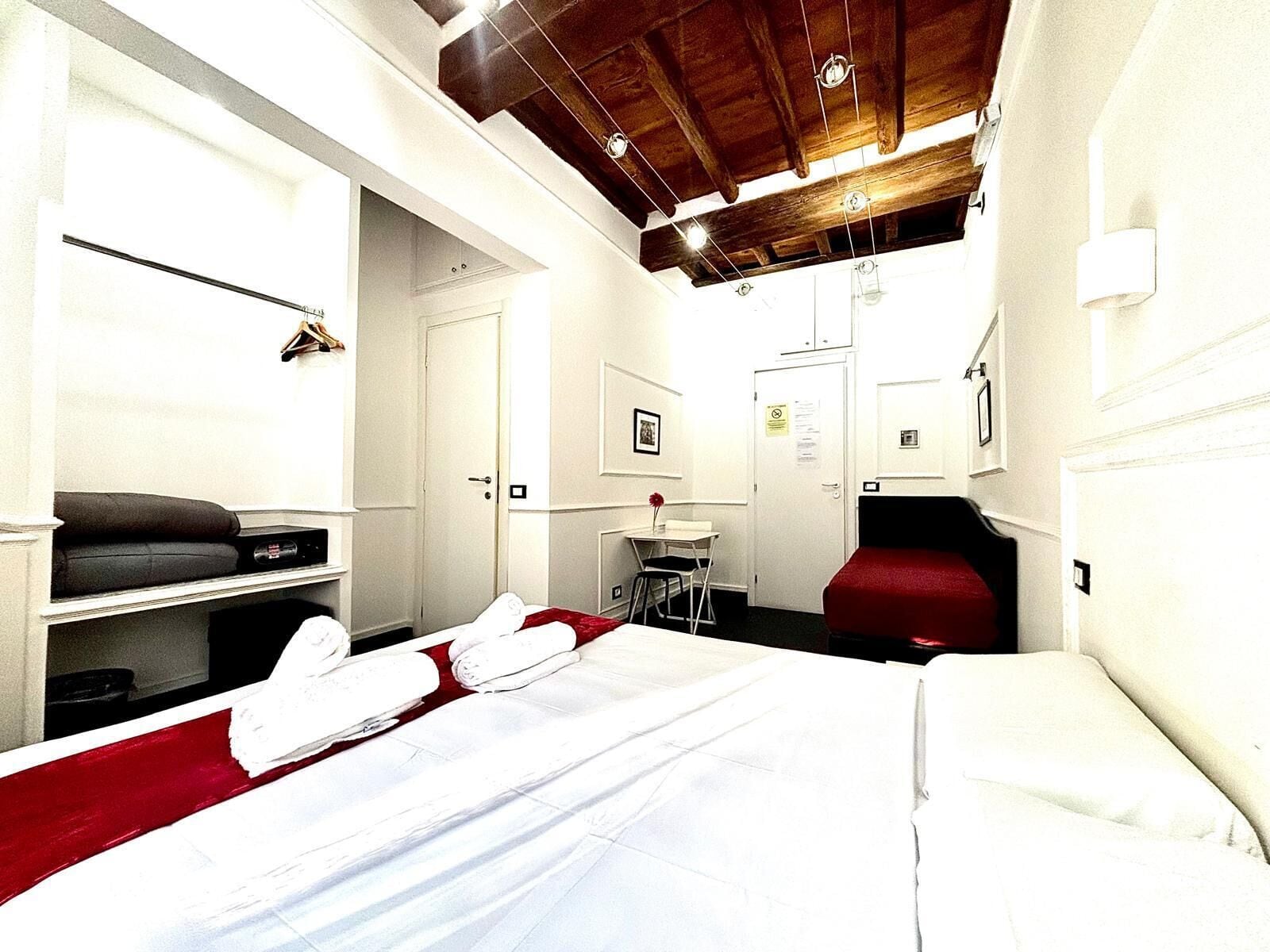 A hotel room with a bed, a desk, a chair, and a red sofa.