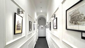 A hallway with framed pictures on the walls, a tiled floor, and a white ceiling with a light fixture. - Antica Locanda dell'Orso (Rome)