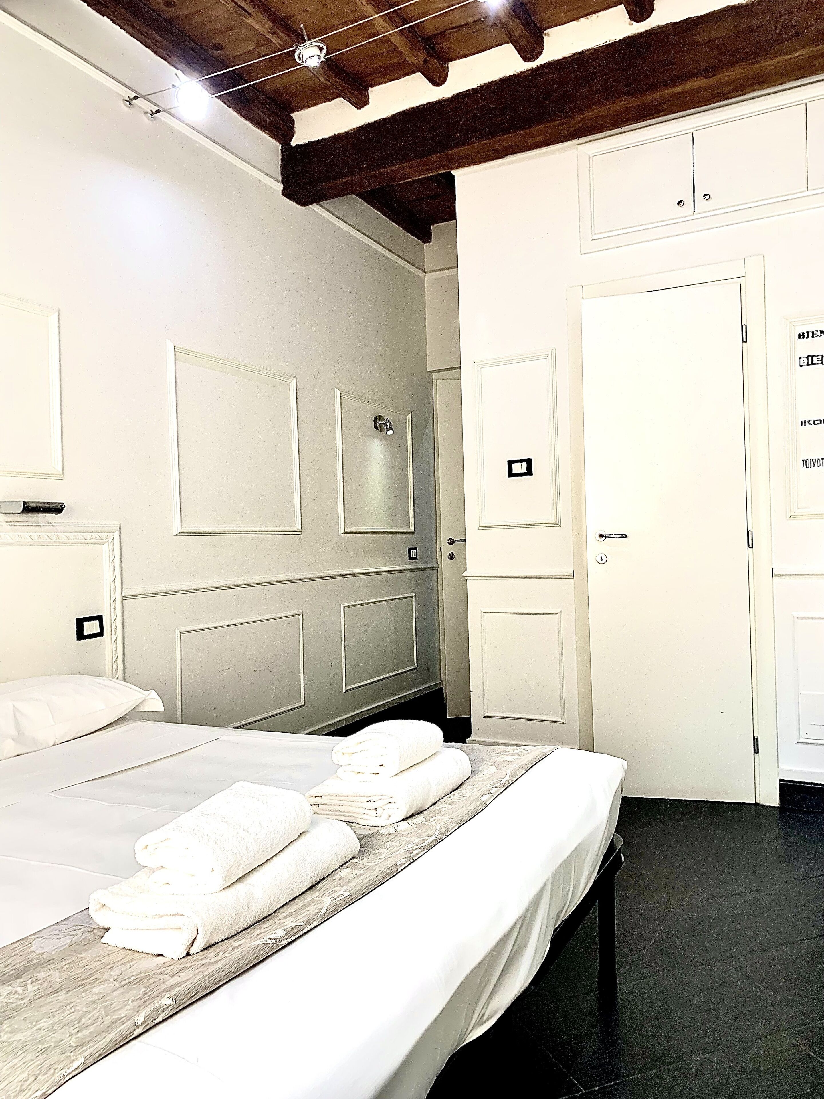 Un dormitorio con cama, cabecera de madera, puerta blanca y techo con vigas a la vista.