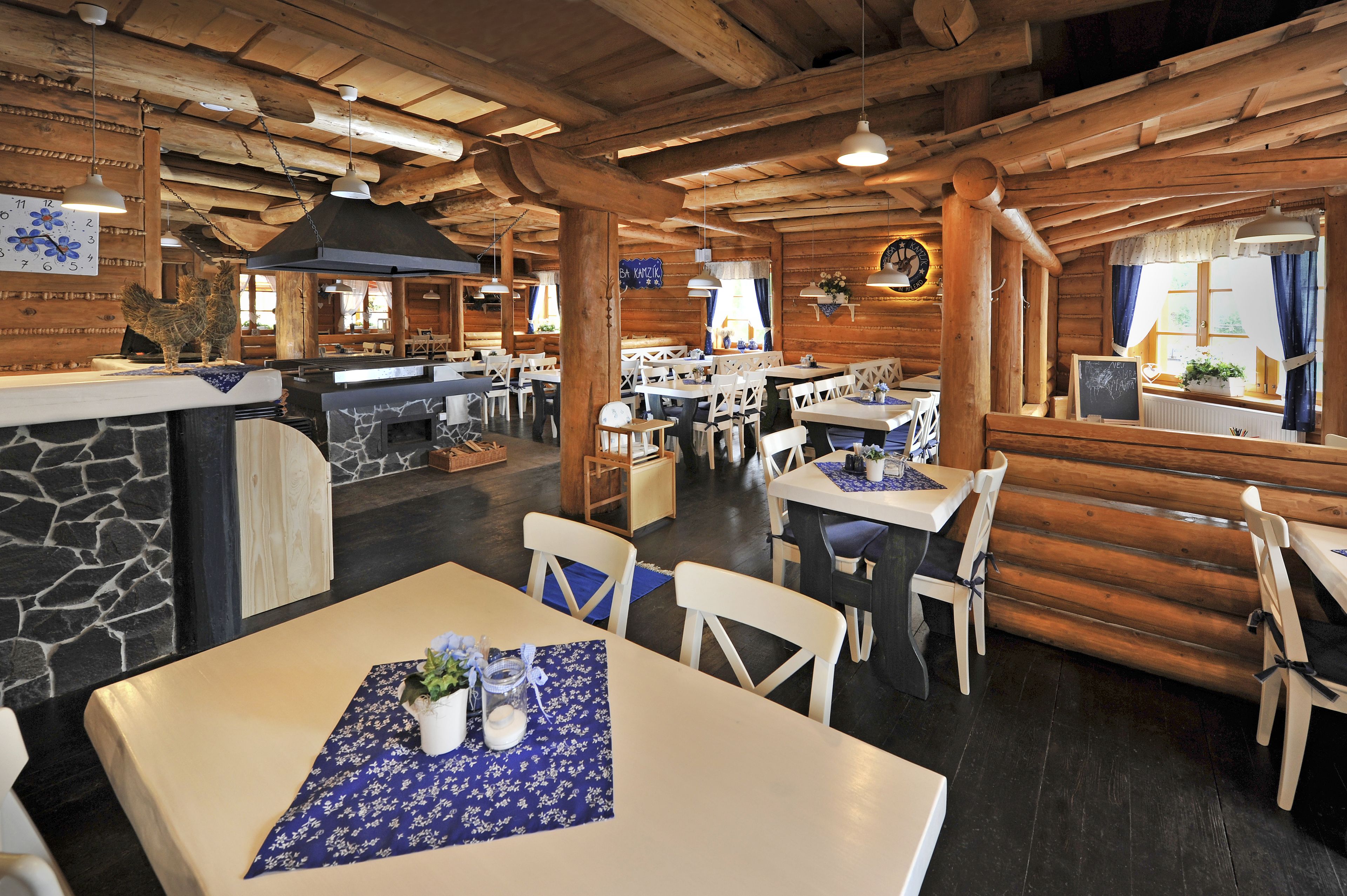 A rustic wooden interior with stone walls, wooden tables, and chairs.