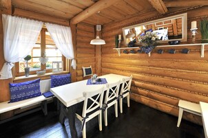Interior de una cabaña de madera con una mesa de comedor, cuatro sillas, un banco con cojines azules, una lámpara colgante y un espejo en la pared.