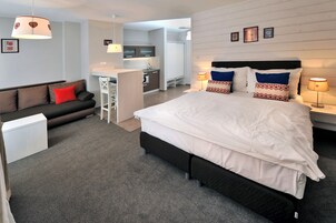 A modern hotel room with a large bed, a sofa, a desk, and a kitchenette.