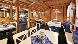 Un restaurante de estilo cabaña de troncos con interiores de madera, mesas y sillas blancas, y una zona de bar central.