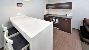 Una cocina moderna con encimera blanca, armarios marrón oscuro, horno empotrado y hervidor.