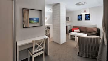 Et moderne, lyst værelse med skrivebord, stol og sofa. Der er et spiseområde med bord og stole, samt kunst på væggene.