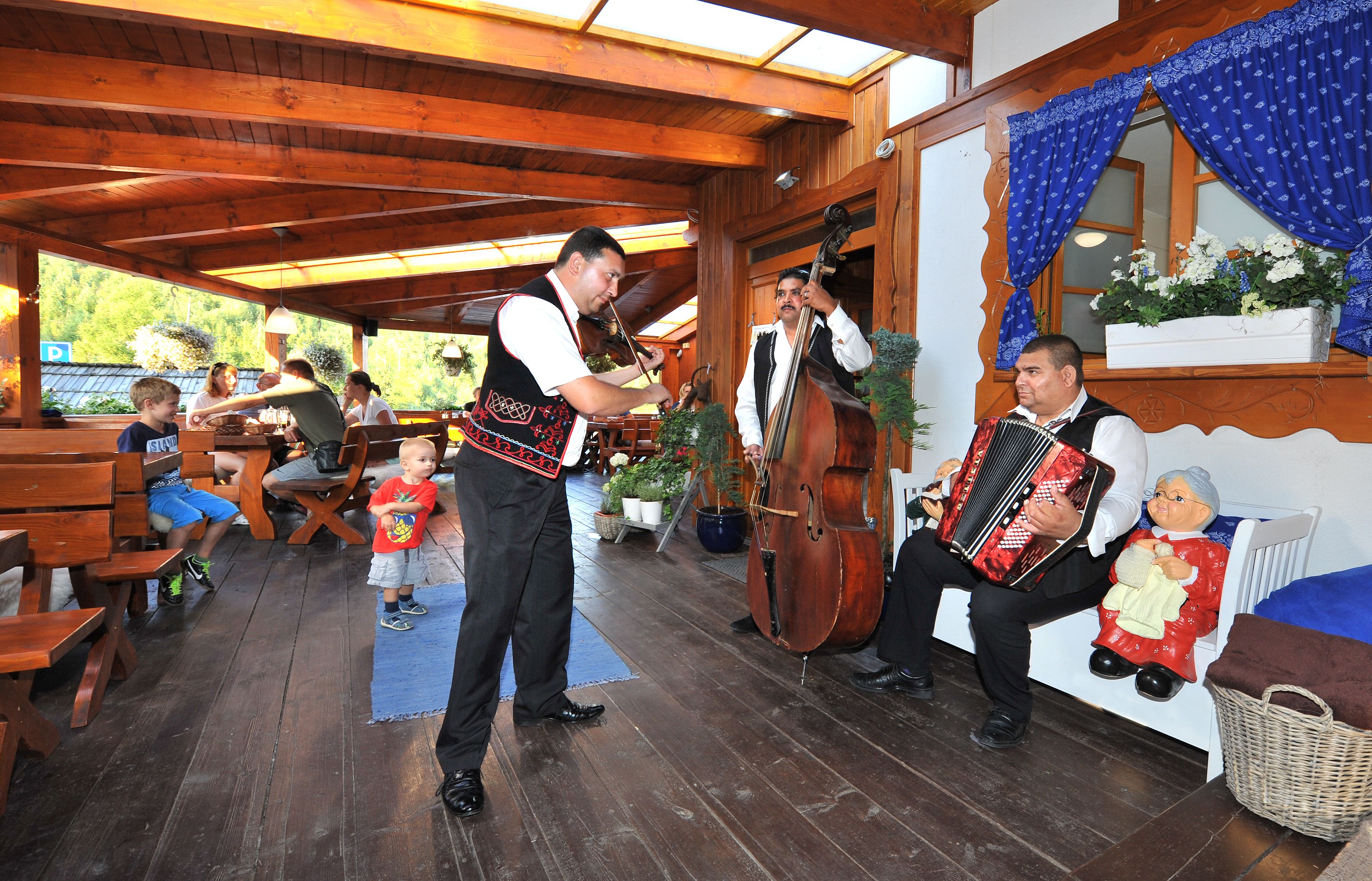 A wooden interior with benches and a table, a man playing a double bass, and another playing an accordion.