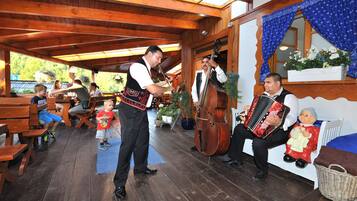 A wooden interior with benches and a table, a man playing a double bass, and another playing an accordion.