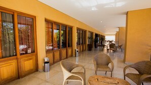 A corridor with wicker furniture and a wooden table, leading to a seating area with chairs and a table. - Hotel Nacional Inn Araxá (Araxá)