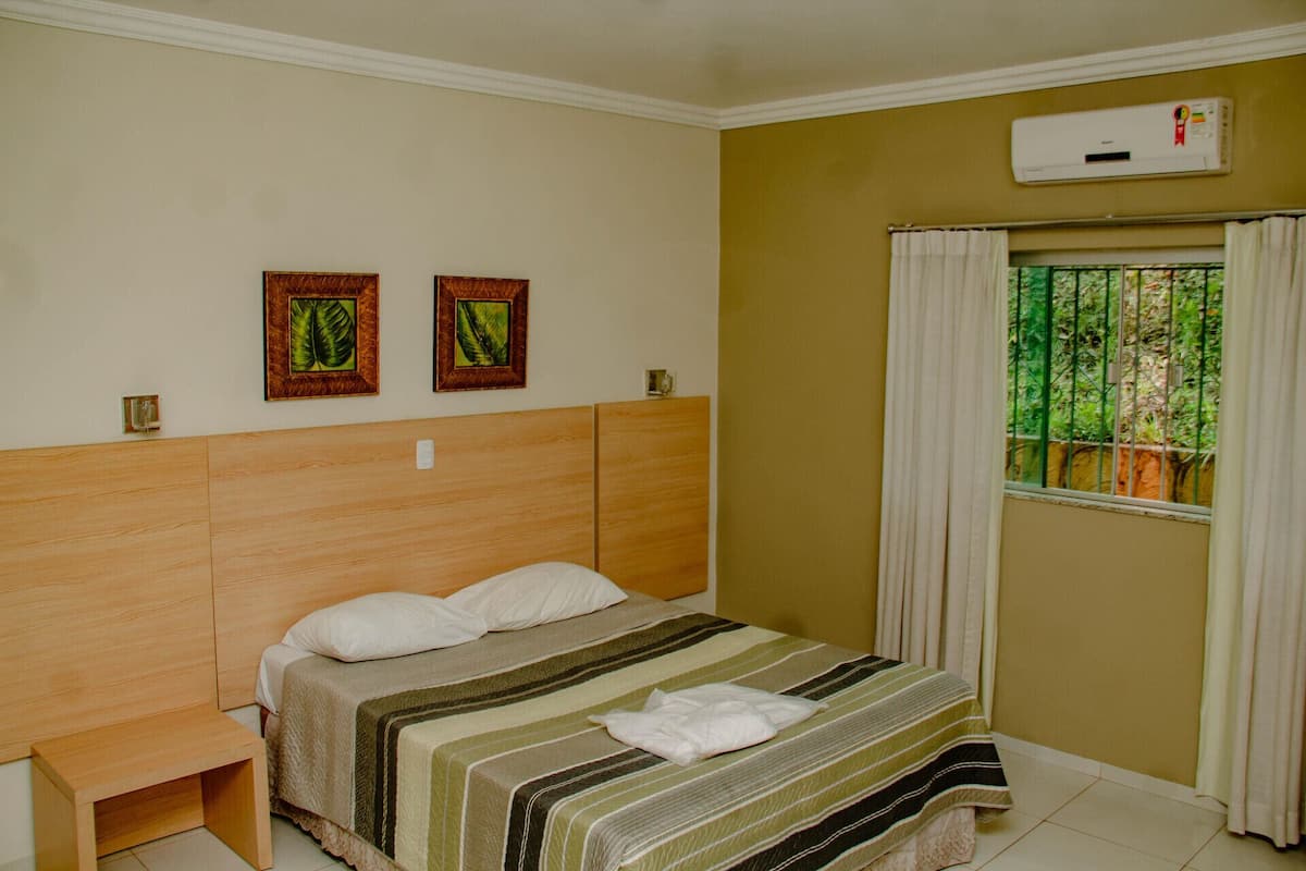 A bedroom with a wooden headboard, a bed with striped bedding, two framed pictures on the wall, and a window with curtains.