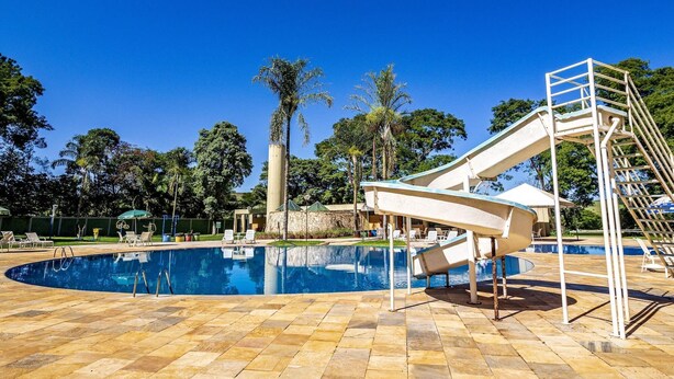 A swimming pool with a slide and a ladder, surrounded by lounge chairs and palm trees. - Hotel Nacional Inn Araxá (Araxá)