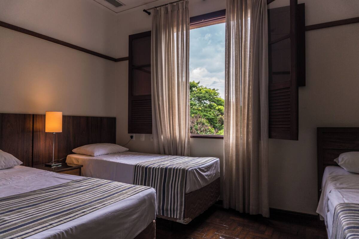 A hotel room with two single beds, a nightstand with a lamp, and a window with curtains.