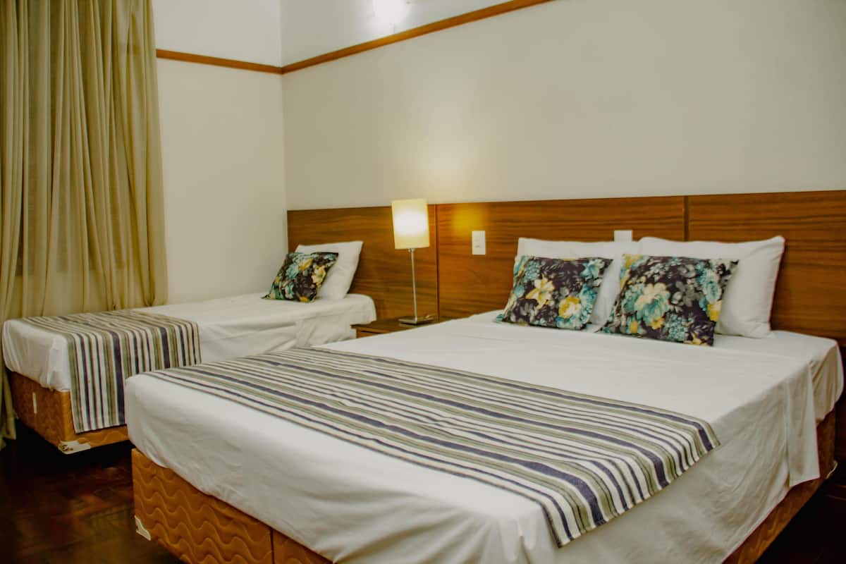 A hotel room with two single beds, wooden headboards, white bedding, and a bedside lamp.