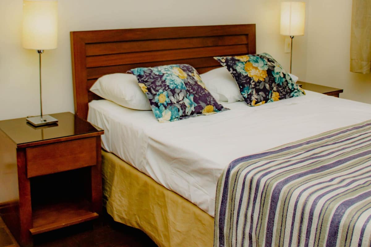 A neatly made bed with a wooden headboard, two bedside lamps, and a striped blanket.