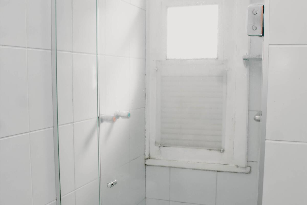 A small, enclosed shower area with a glass door, a window, and a toilet paper holder on the wall.