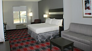Hotelkamer met een bed, een bank, een salontafel, een bureau en een stoel. Er is een raam met zonwering, een lamp en een schilderij aan de muur.