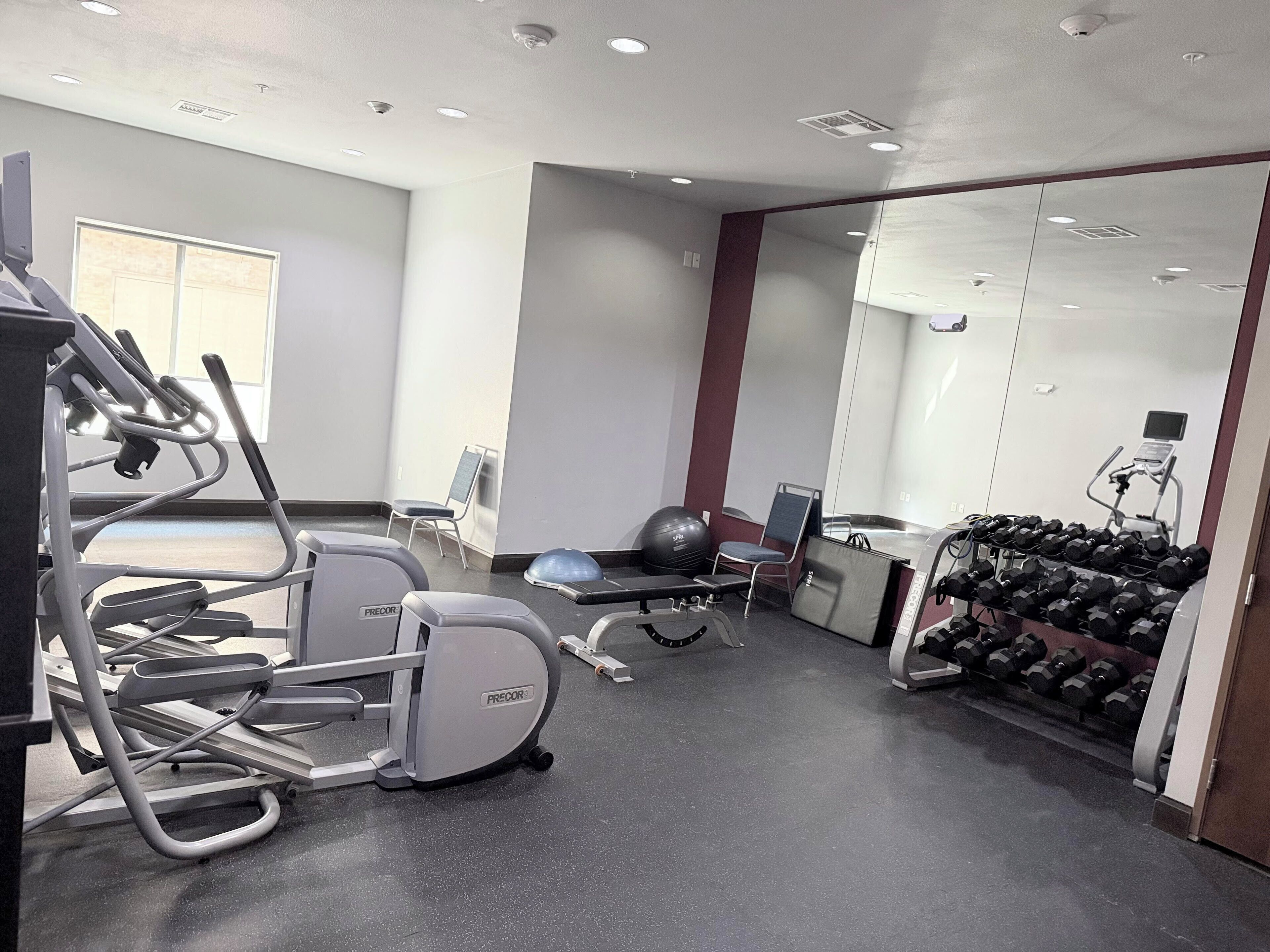 A gym with treadmills, elliptical machines, a stationary bike, and a rack of dumbbells.