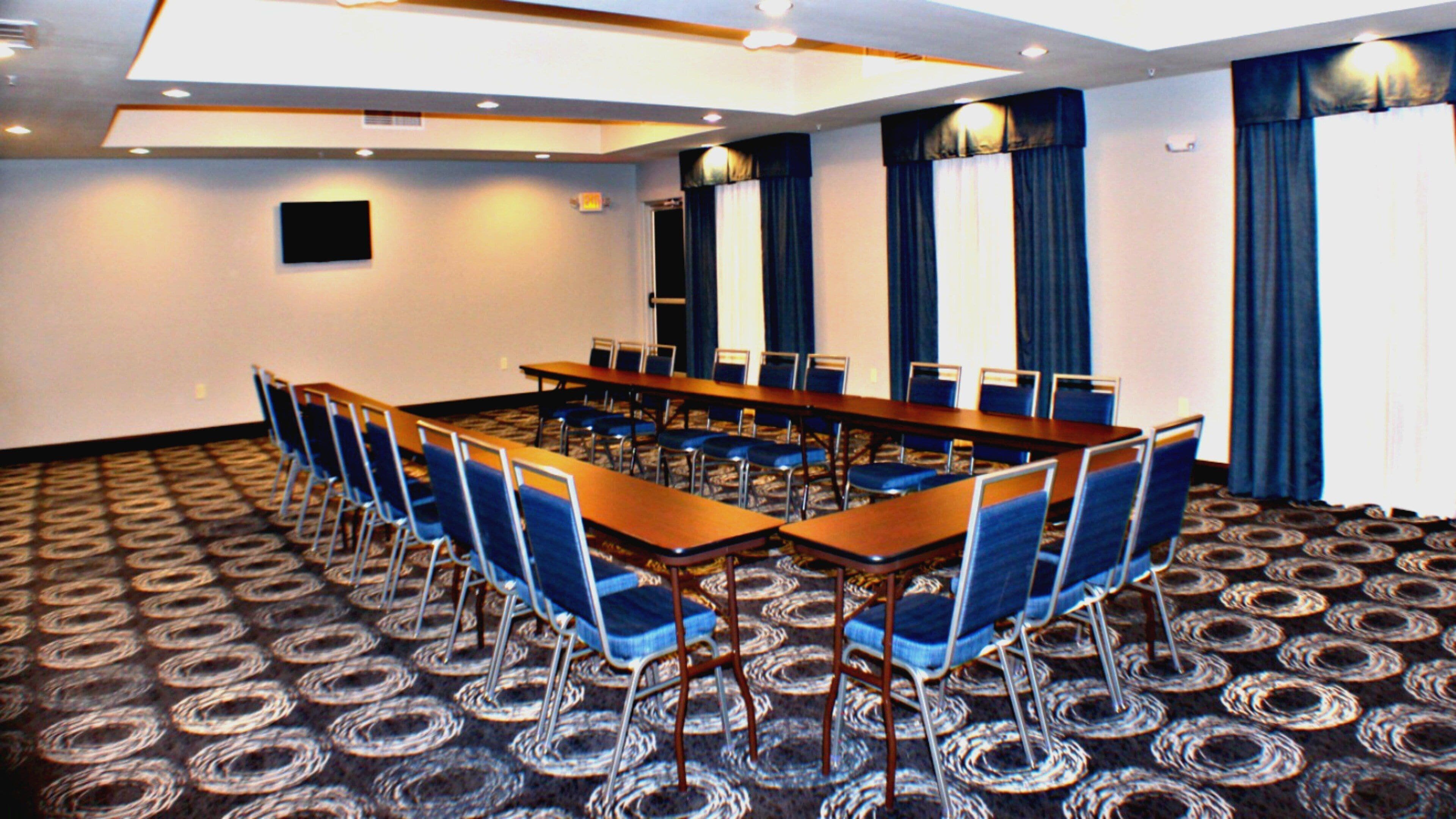 A conference room with a long table and chairs, carpeted floor, and large windows with curtains.