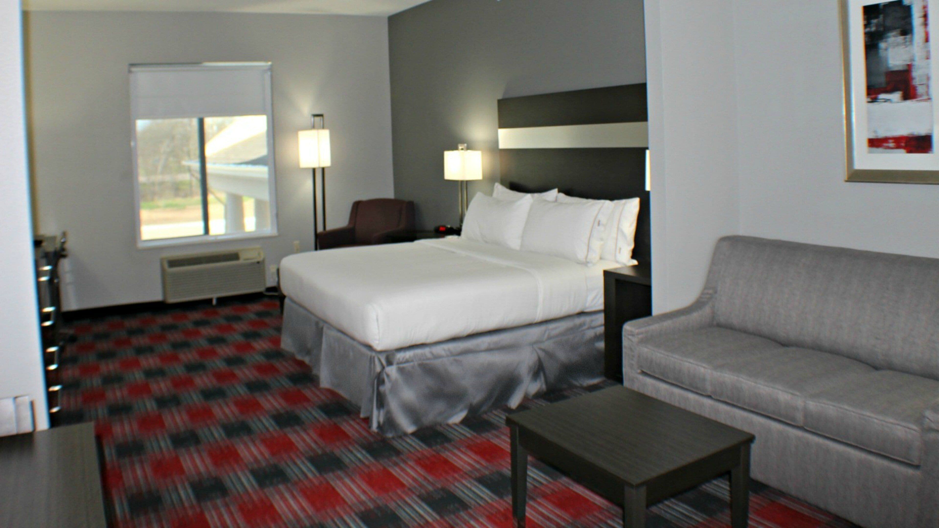A hotel room with a bed, a sofa, a coffee table, a desk, and a lamp.