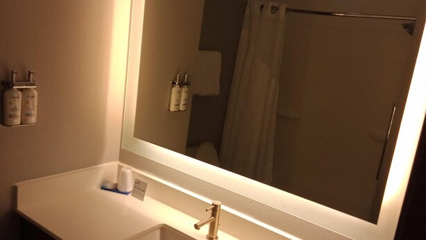 A bathroom with a large mirror, a sink, and toiletries on the wall. - Holiday Inn Express & Suites Bonham by IHG (Bonham)