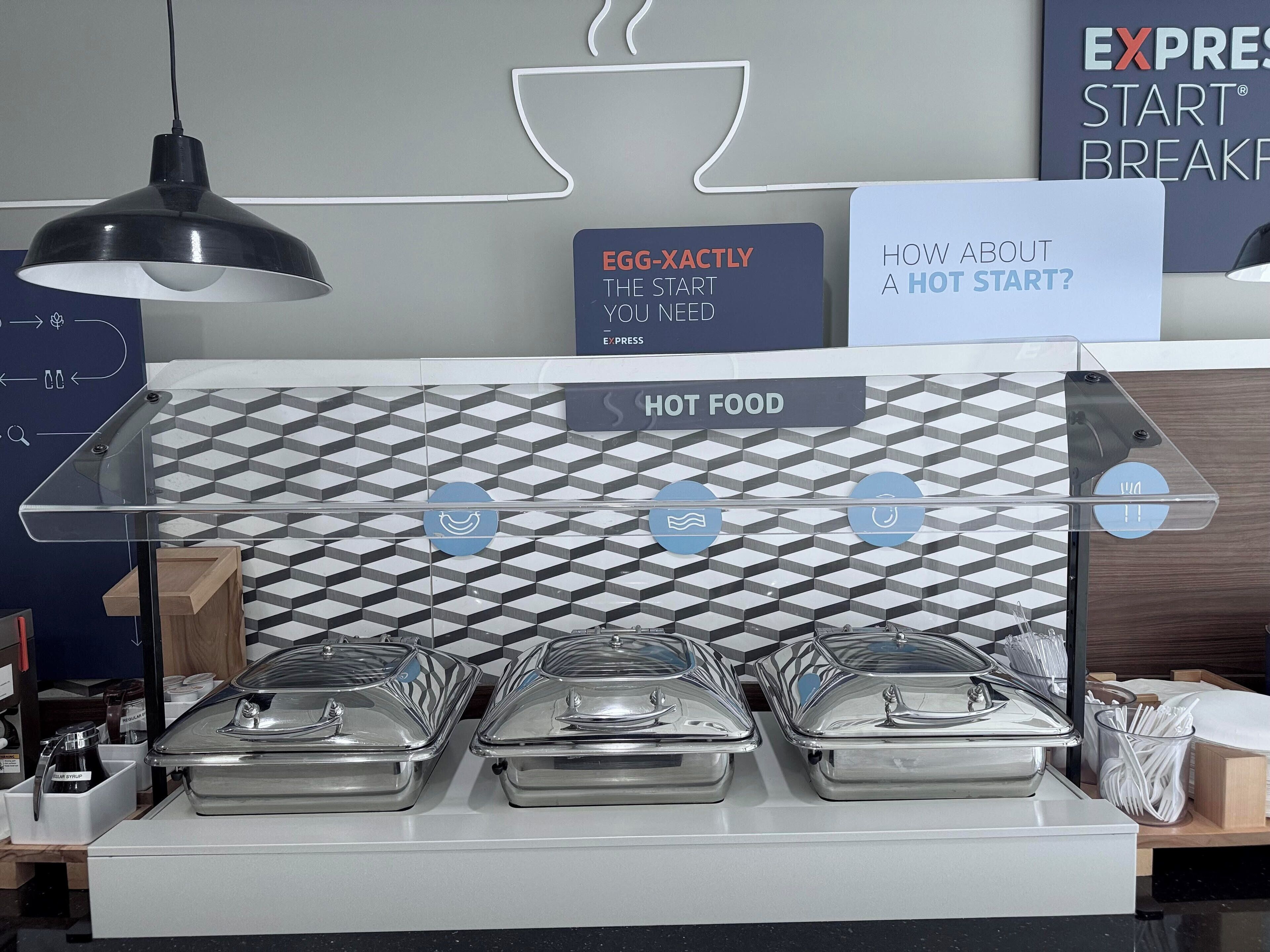 Un buffet bien organisé, avec une signalétique claire indiquant les plats chauds proposés et un espace dédié au café, arborant le logo de la marque.