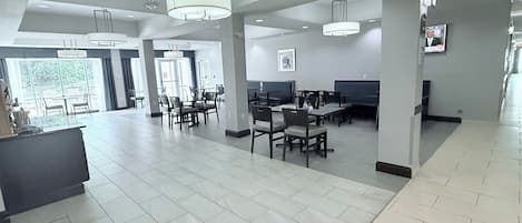Un amplio vestíbulo de hotel con techos altos, candelabros modernos y una zona de estar central con mesas y sillas.