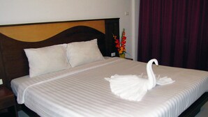 A neatly made bed with a swan-shaped pillow and a vase of flowers on the nightstand. - Nina's Guest House 2 (Patong)