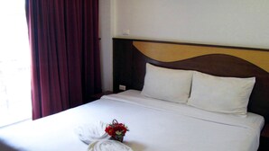 A hotel room with a bed, a wooden headboard, and a window with curtains. - Nina's Guest House 2 (Patong)
