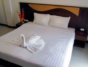 A neatly made bed with a swan-shaped towel in the center, a wooden headboard, and a nightstand with a vase of flowers. - Nina's Guest House 2 (Patong)
