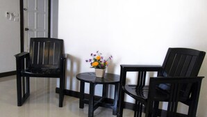 A room with two black chairs, a small round table, and a potted plant with flowers. - Nina's Guest House 2 (Patong)