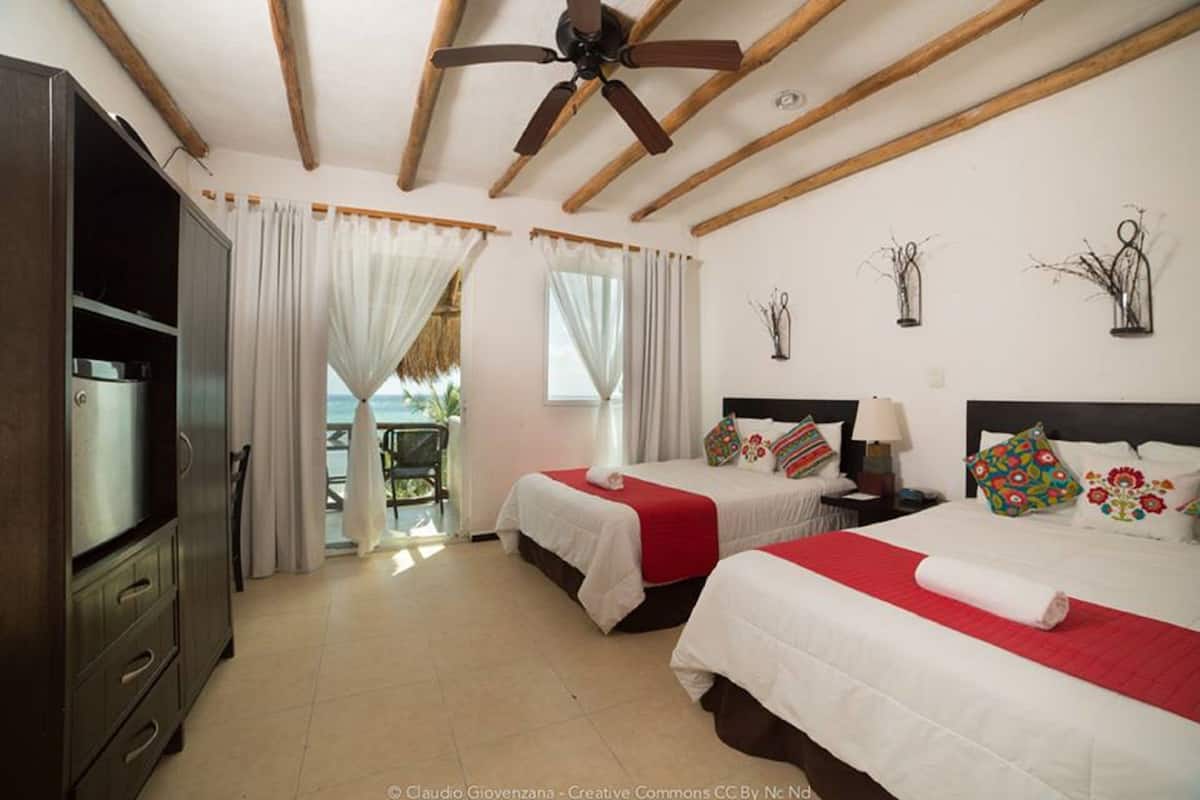 Une chambre d’hôtel avec deux lits, un ventilateur de plafond, une télévision et un balcon avec des rideaux.