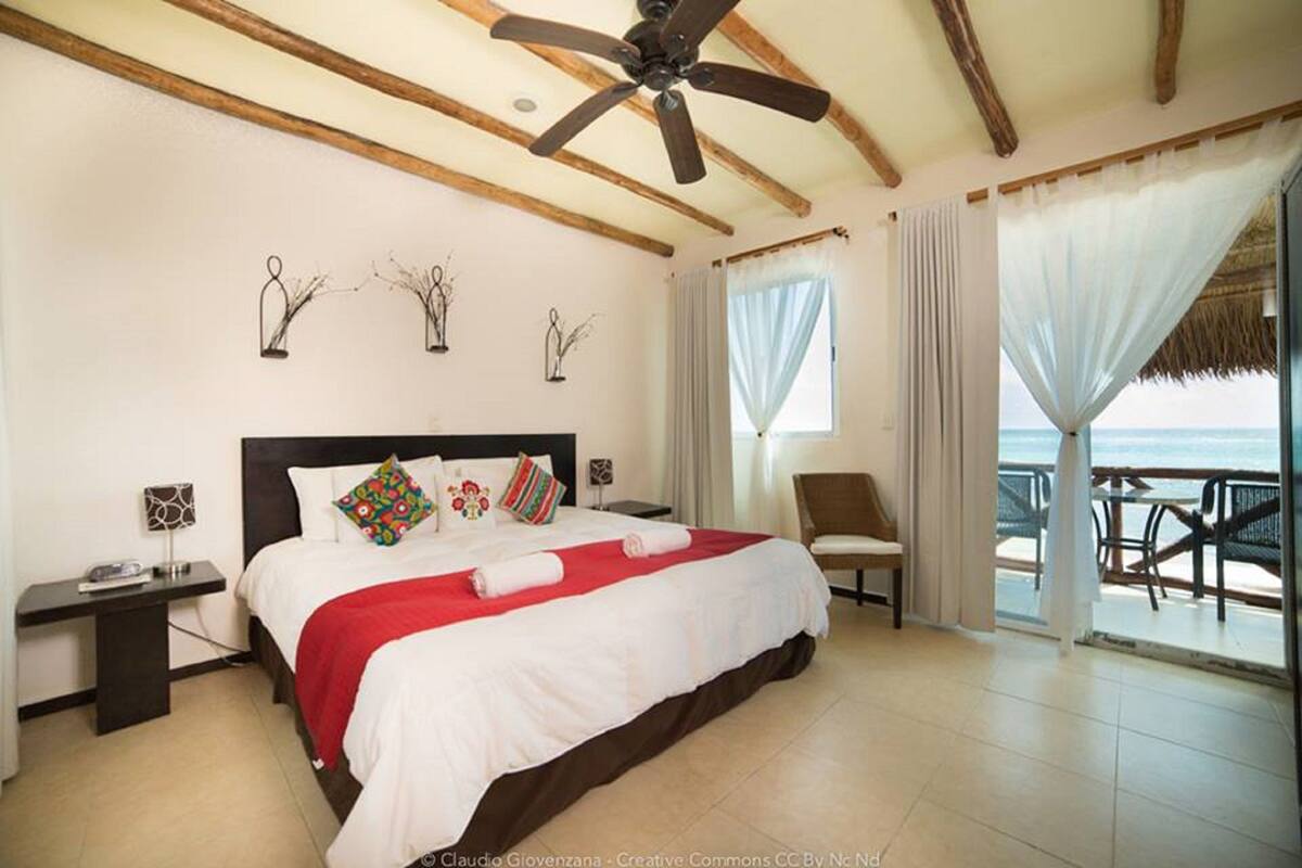 Une chambre à coucher comprenant un lit, un bureau, une chaise, un ventilateur de plafond et un balcon avec vue sur la mer.