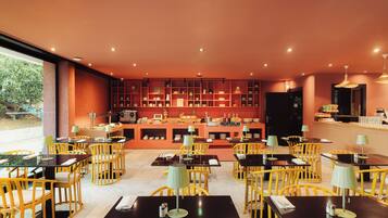 A restaurant with yellow chairs and black tables, a bar area, and a view of greenery outside.