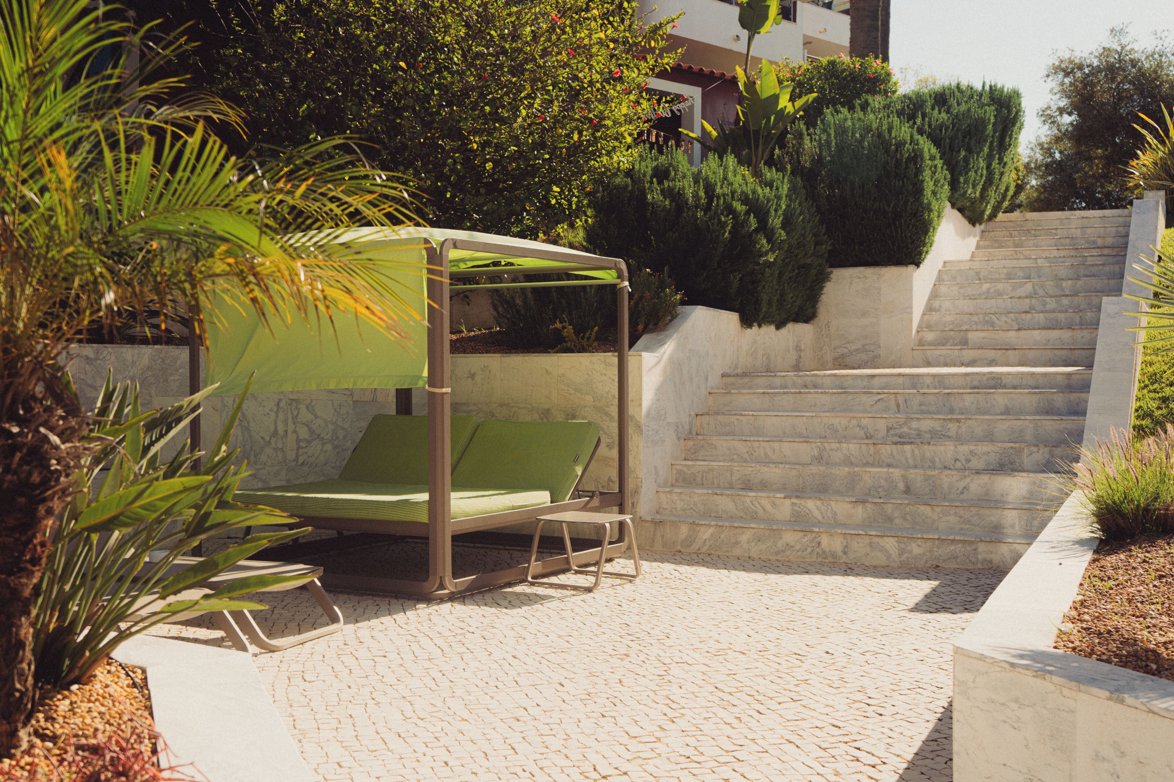 Un espace extérieur abrité avec des sièges, comprenant une chaise et une petite table, un chemin pavé et un escalier menant à un niveau supérieur.