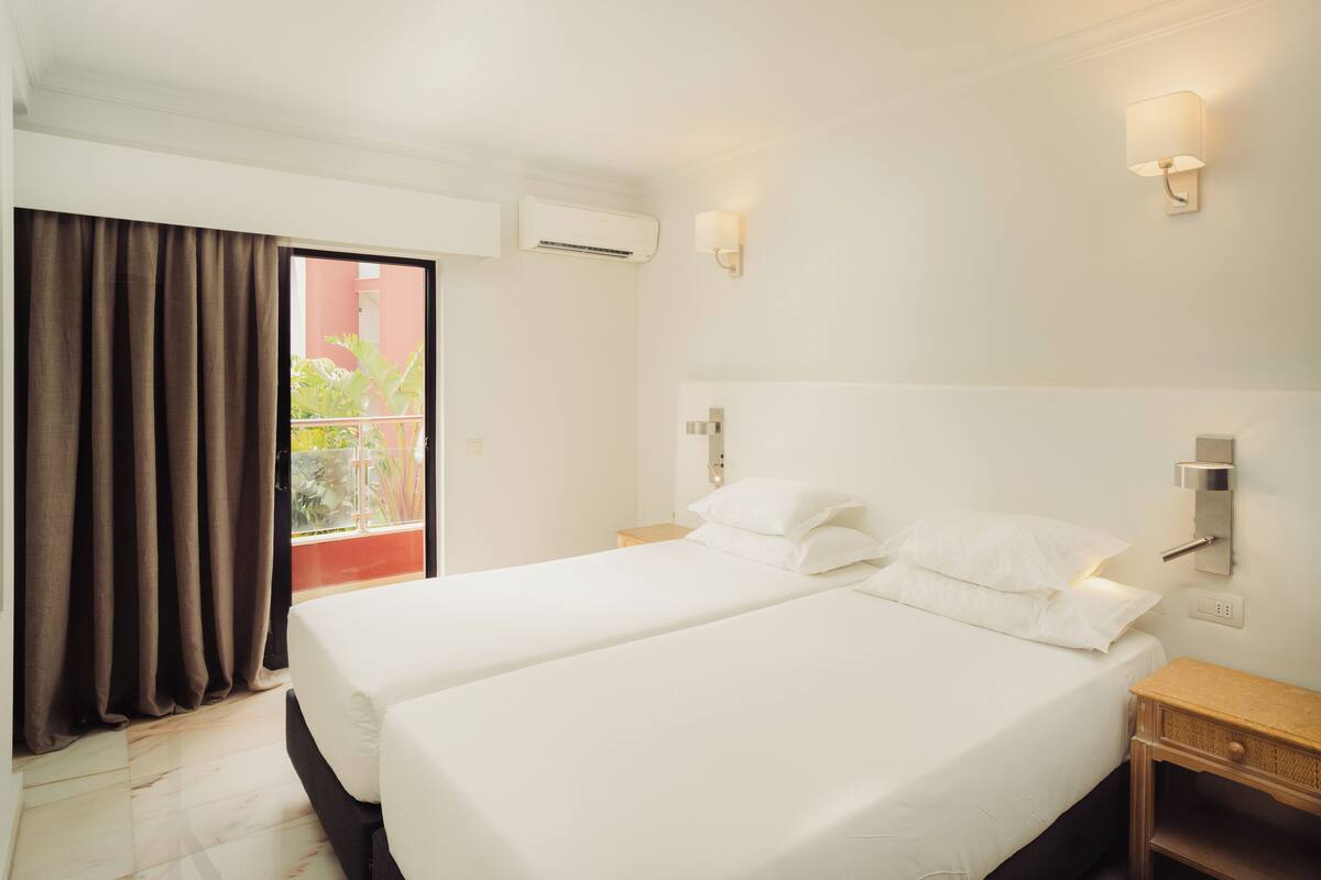 Hotelkamer met twee bedden, een balkon met gordijnen, een airconditioning en wandlampen.