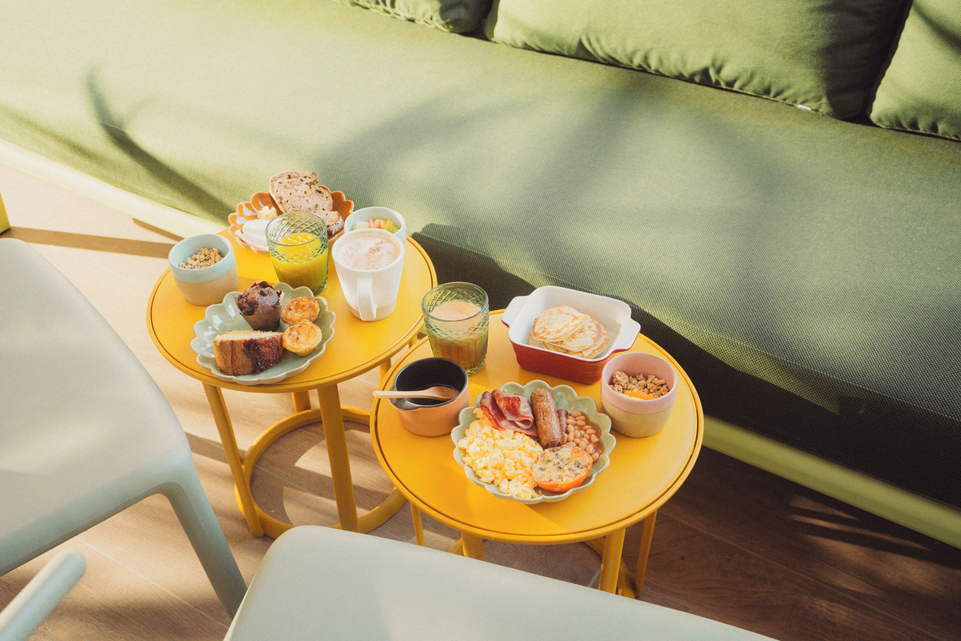 Colazione servita su un tavolo giallo, con diversi cibi e un bicchiere di succo d'arancia.