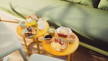 A breakfast setup on a yellow table with various food items and a glass of orange juice.