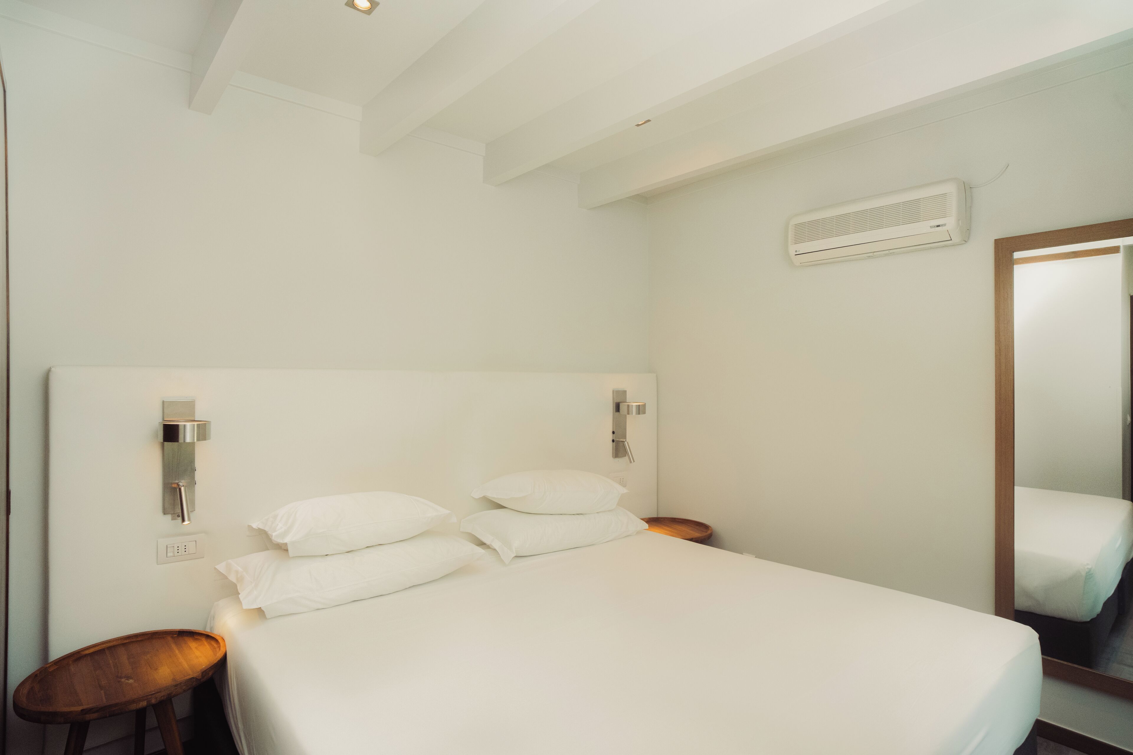 Un dormitorio con cama, mesitas de noche, aire acondicionado instalado en la pared y un espejo.