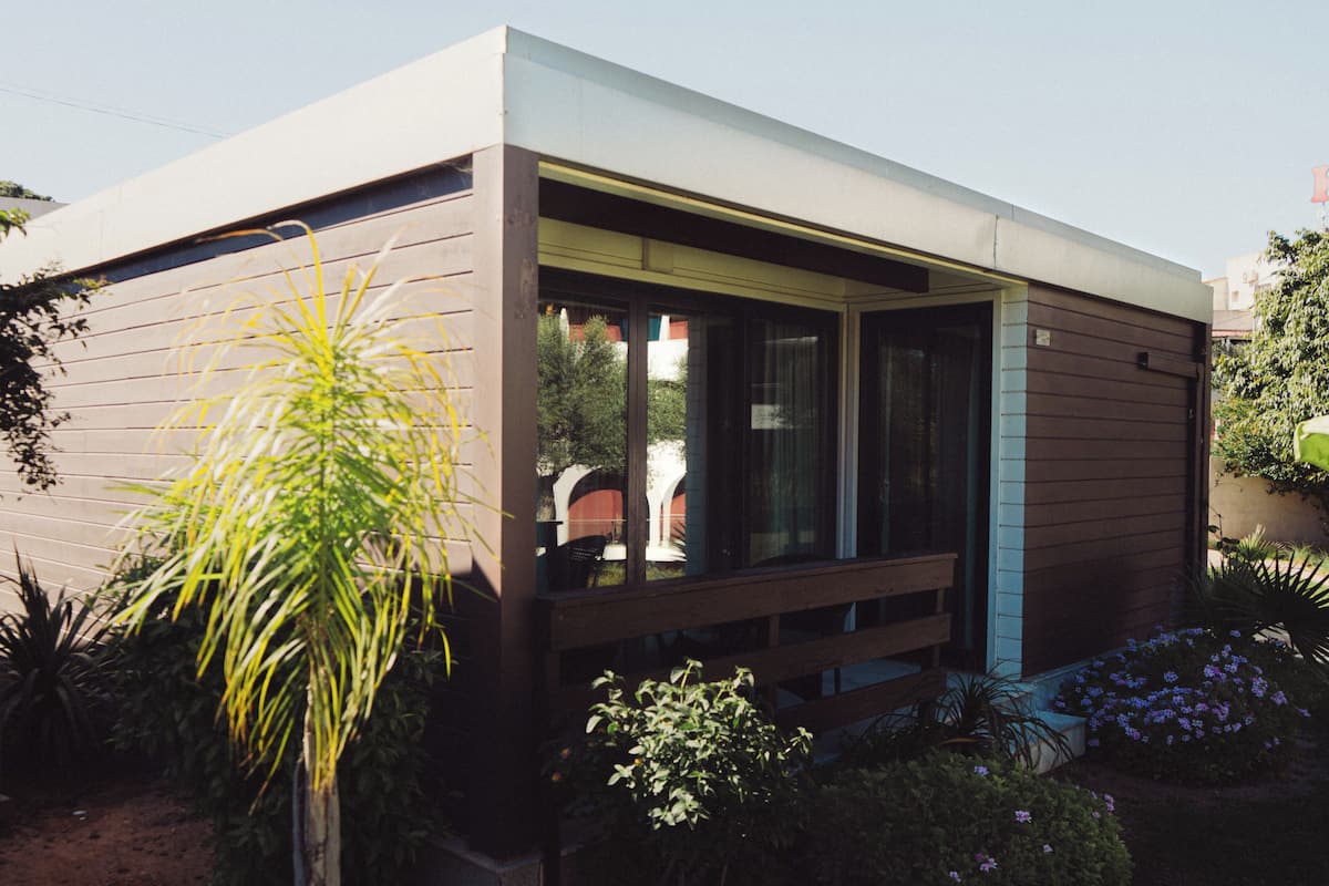 Een modern huis met een groot raam, een houten terras en een tuin met verschillende planten.