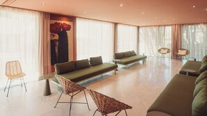 En moderne hotellobby med en grøn sofa, fletstole og et stort maleri på væggen.