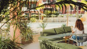 Et udendørs opholdsområde med sofa og stole, omgivet af planter og udsigt til en pool.