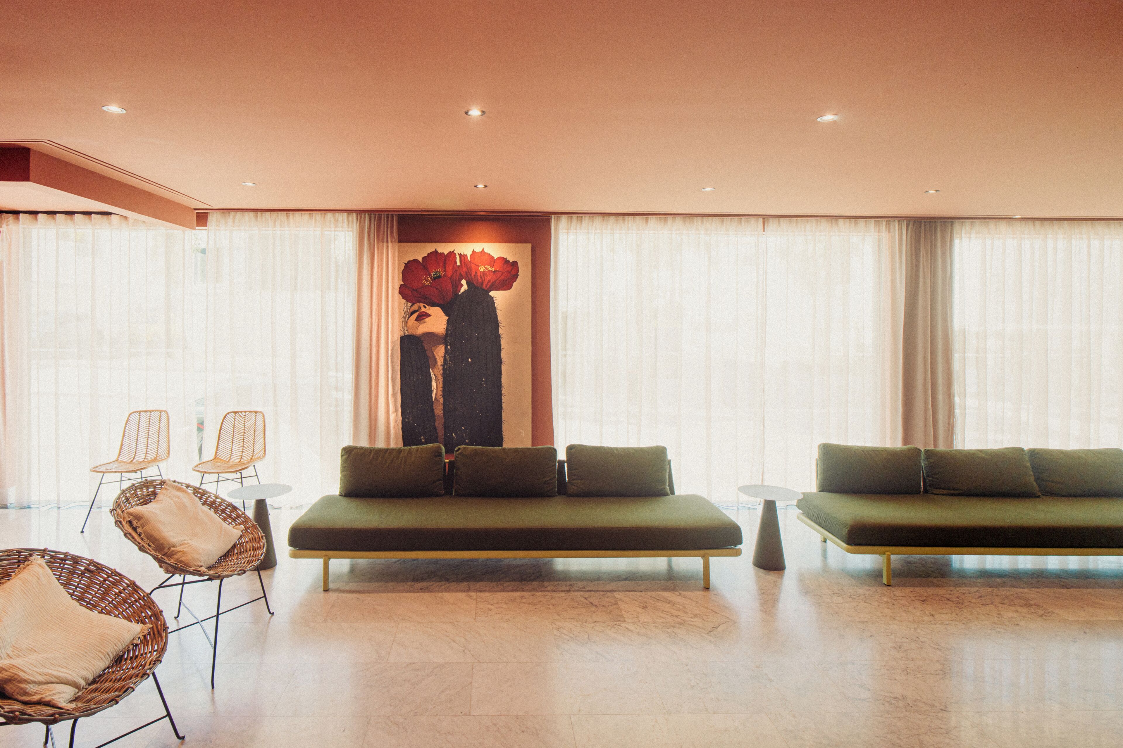 Un salon moderne avec deux canapés, des fauteuils en osier et un grand tableau abstrait.