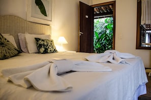 A neatly made bed with white linens and towels, a bedside lamp, and a framed picture on the wall.