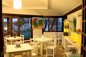 Un comedor con mobiliario blanco, un cuadro y vistas al exterior.