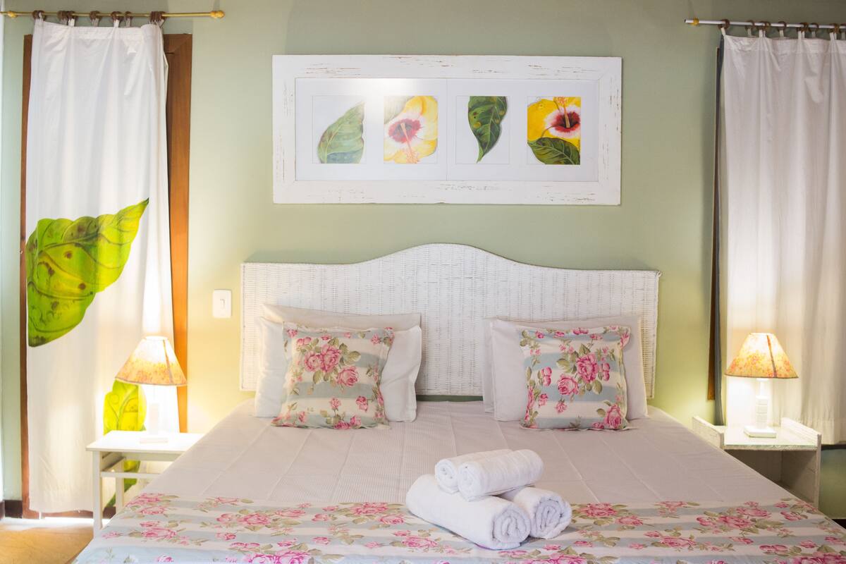 A neatly made bed with floral bedding, two pillows, and rolled towels.