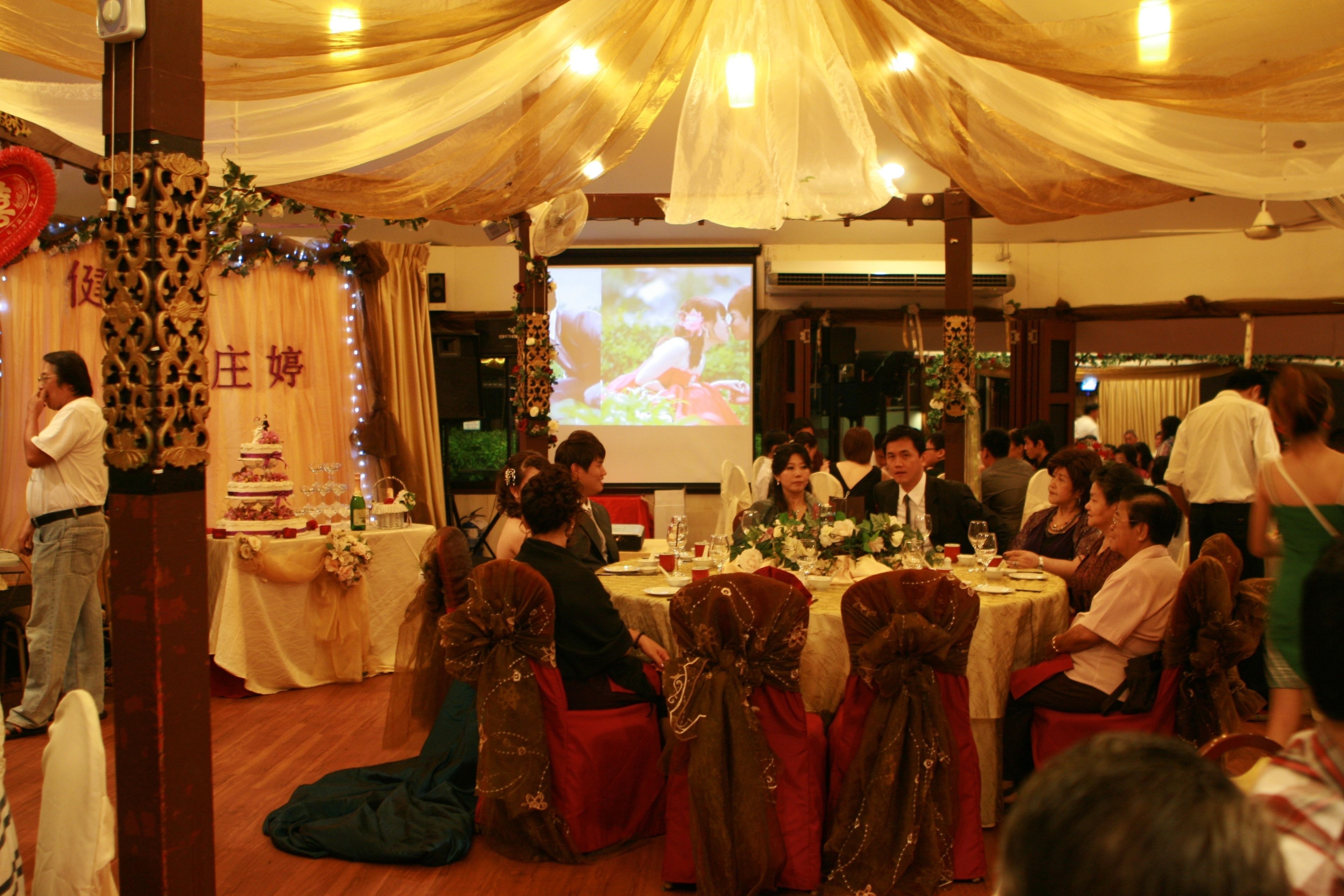 A banquet hall with round tables, guests seated, and a stage with a screen.