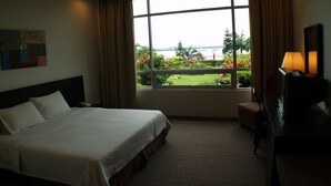 Habitación de hotel con una cama grande, un escritorio, una silla y una ventana con vistas a zonas verdes y agua.